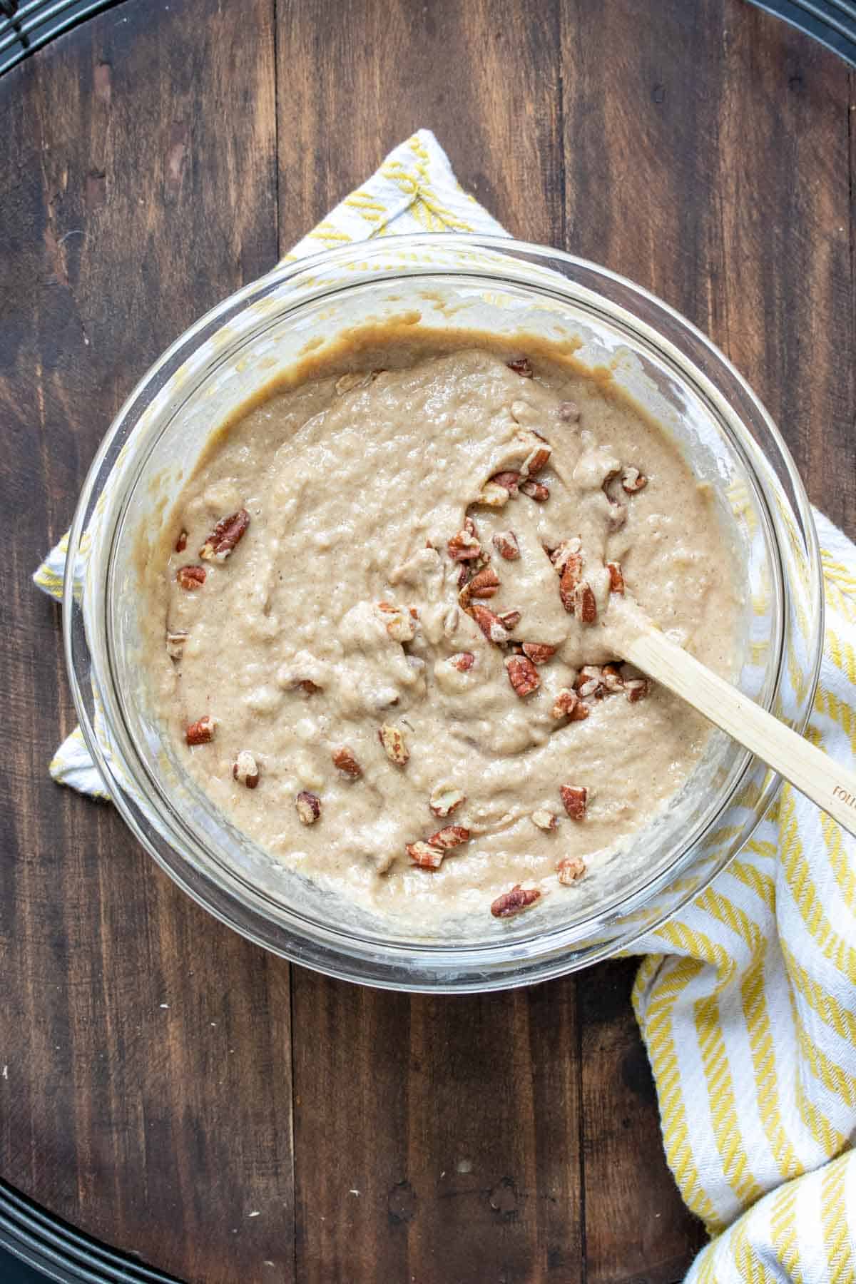 Wooden spoon mixing a tan colored batter with nuts