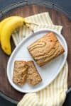 Top view of a white plate with a loaf of banana bread being sliced