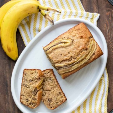 Top view of a white plate with a loaf of banana bread being sliced