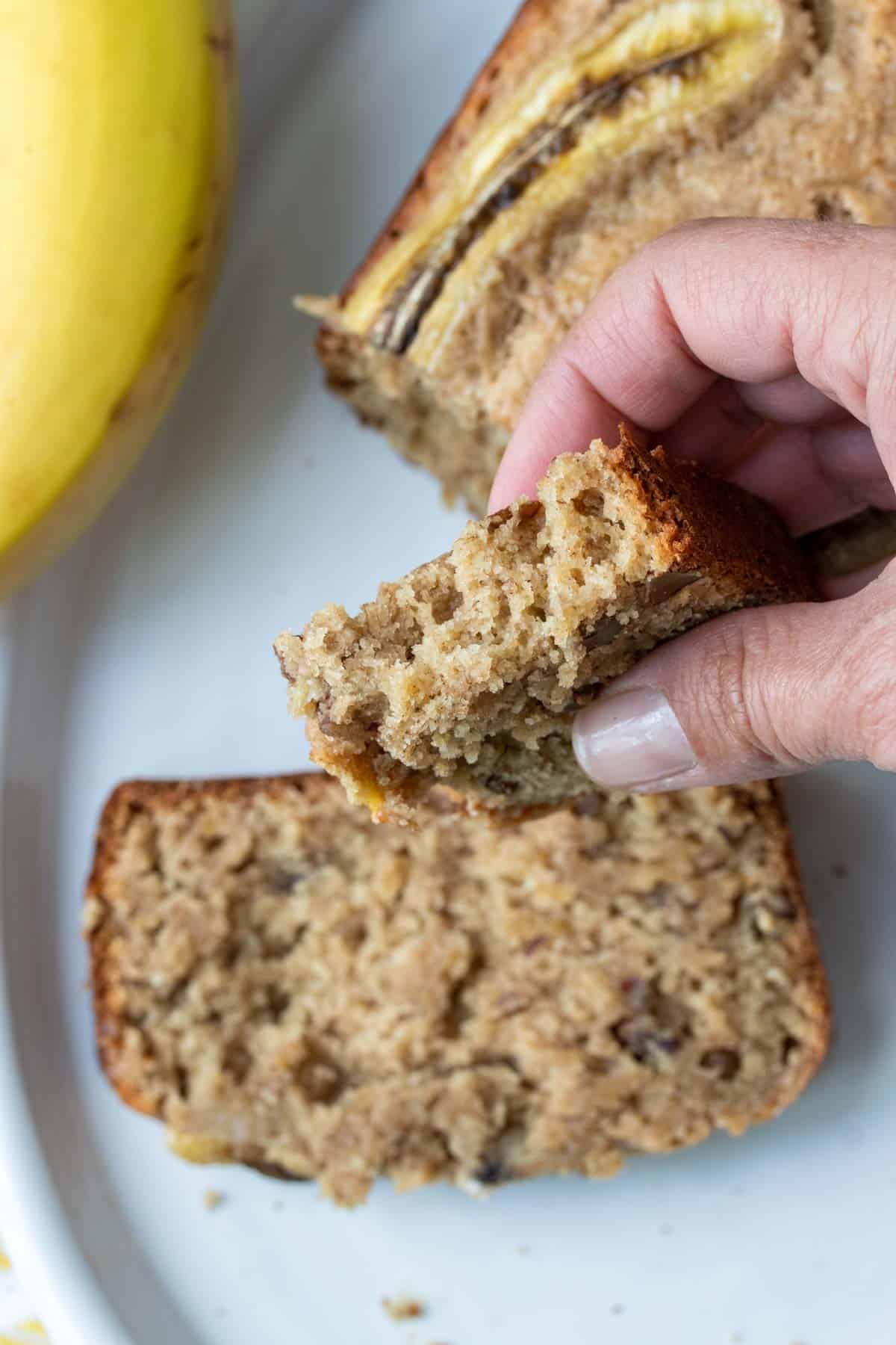 Hand holding half a piece of banana bred over a whole piece