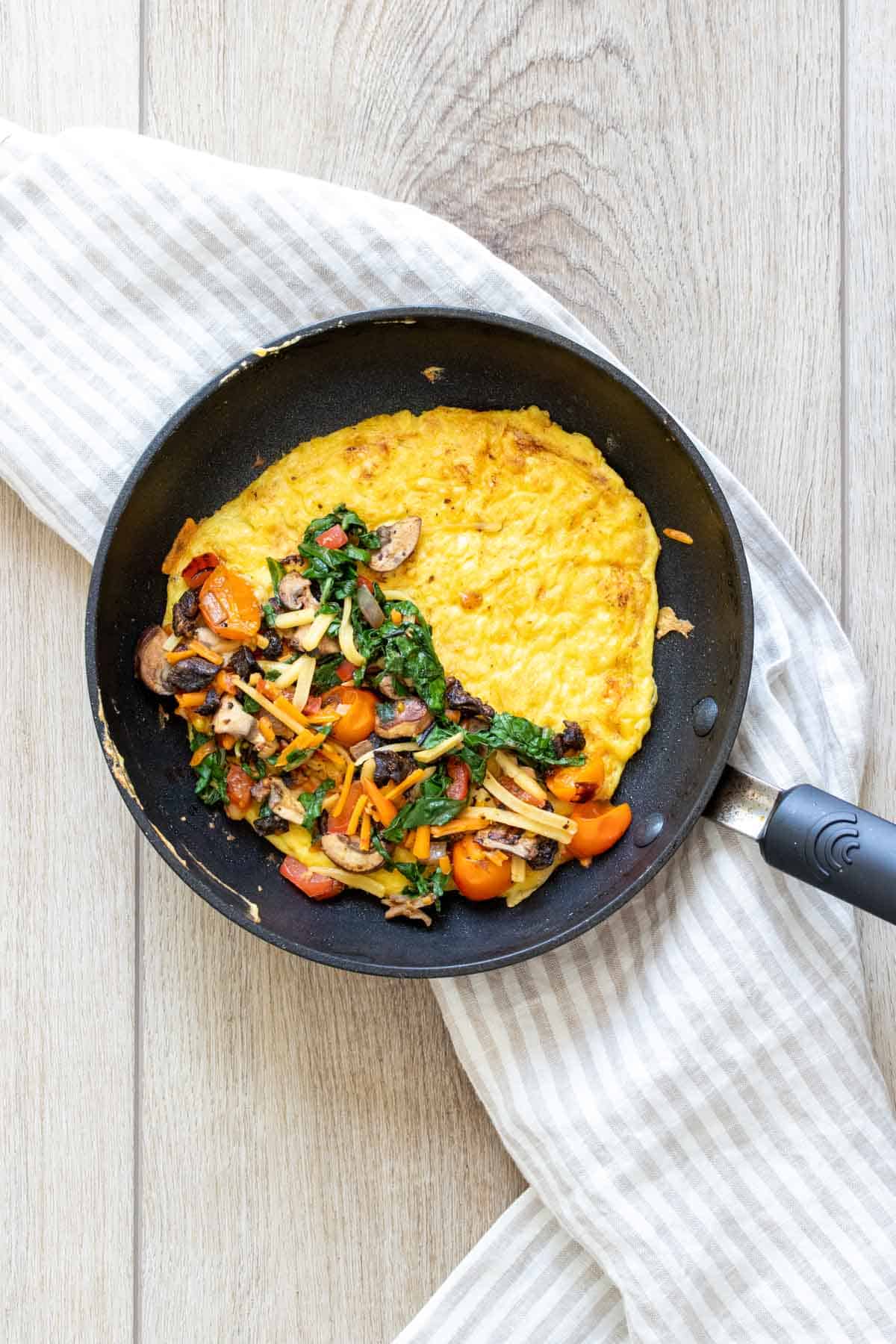 Black pan with an open faced omelet in it and veggies on half of it.