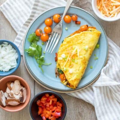 A blue plate on a striped towel with a veggie omelet on it and little bowls of veggies around