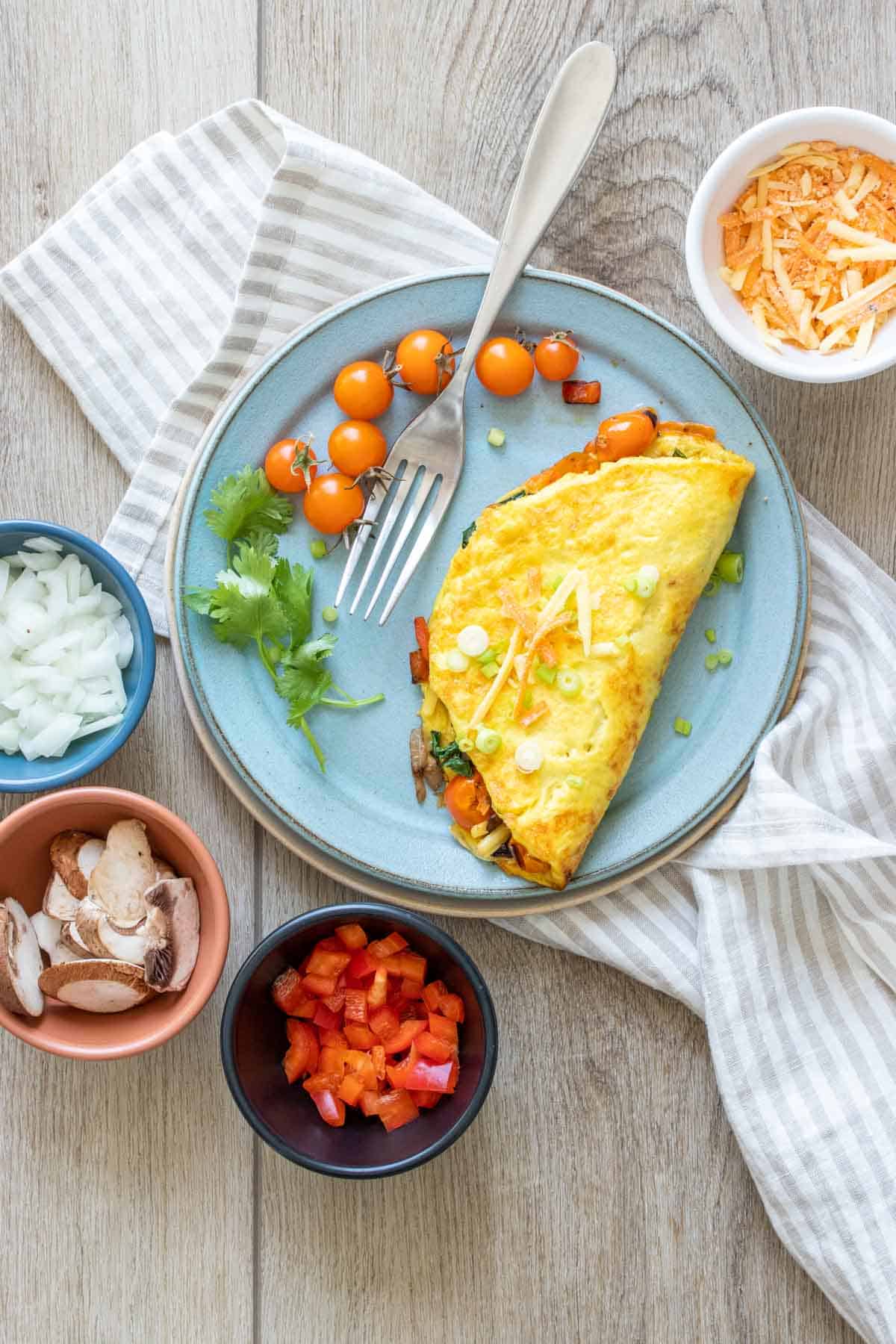 A blue plate on a striped towel with a veggie omelet on it and little bowls of veggies around