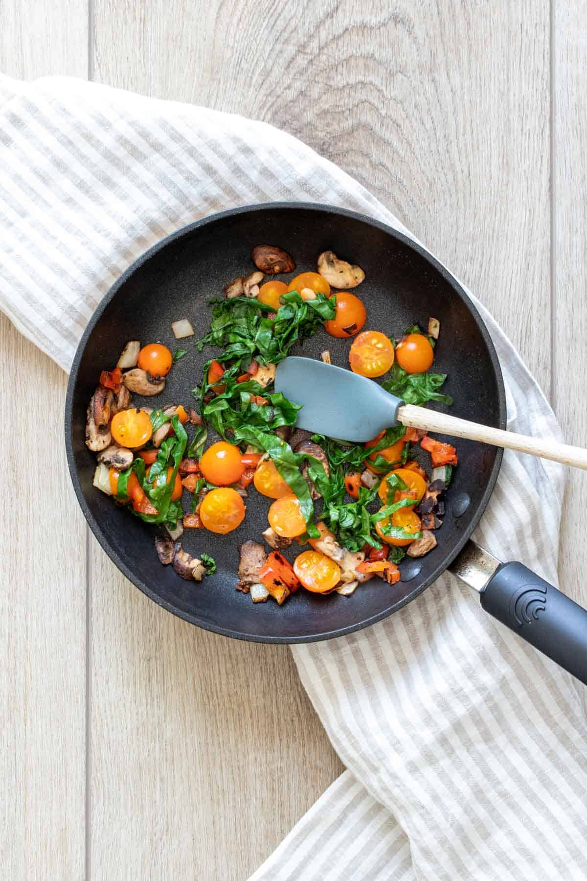 Grey spatula mixing sautéed veggies in a black pan.