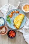 A photo of a veggie omelet on a blue plate with cherry tomatoes and ingredients around it.