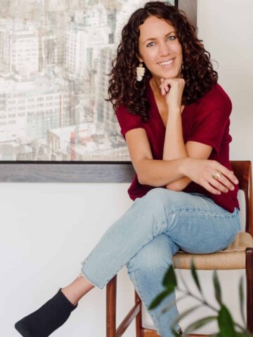 Woman with brown curly hair wearing jeans and a shirt sitting on a chair