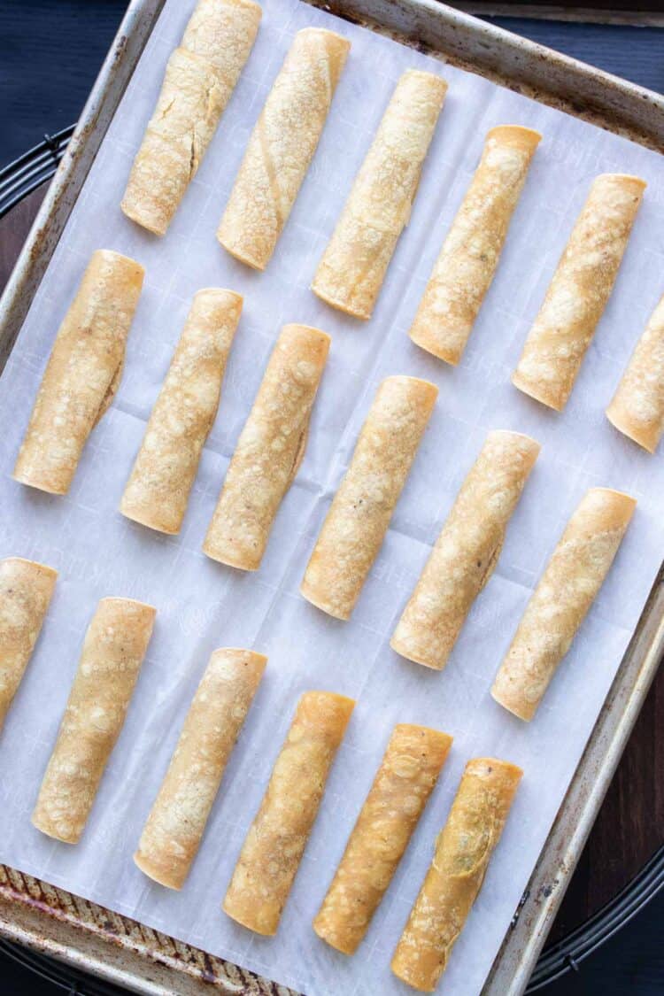 A parchment lined baking sheet topped with rows of unbaked taquitos
