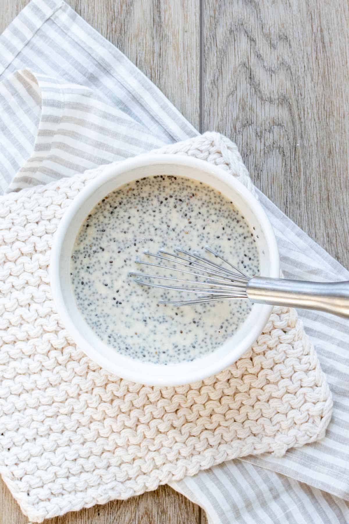 A chia seed milk mixture in a white bowl sitting on a cream towel being whisked.