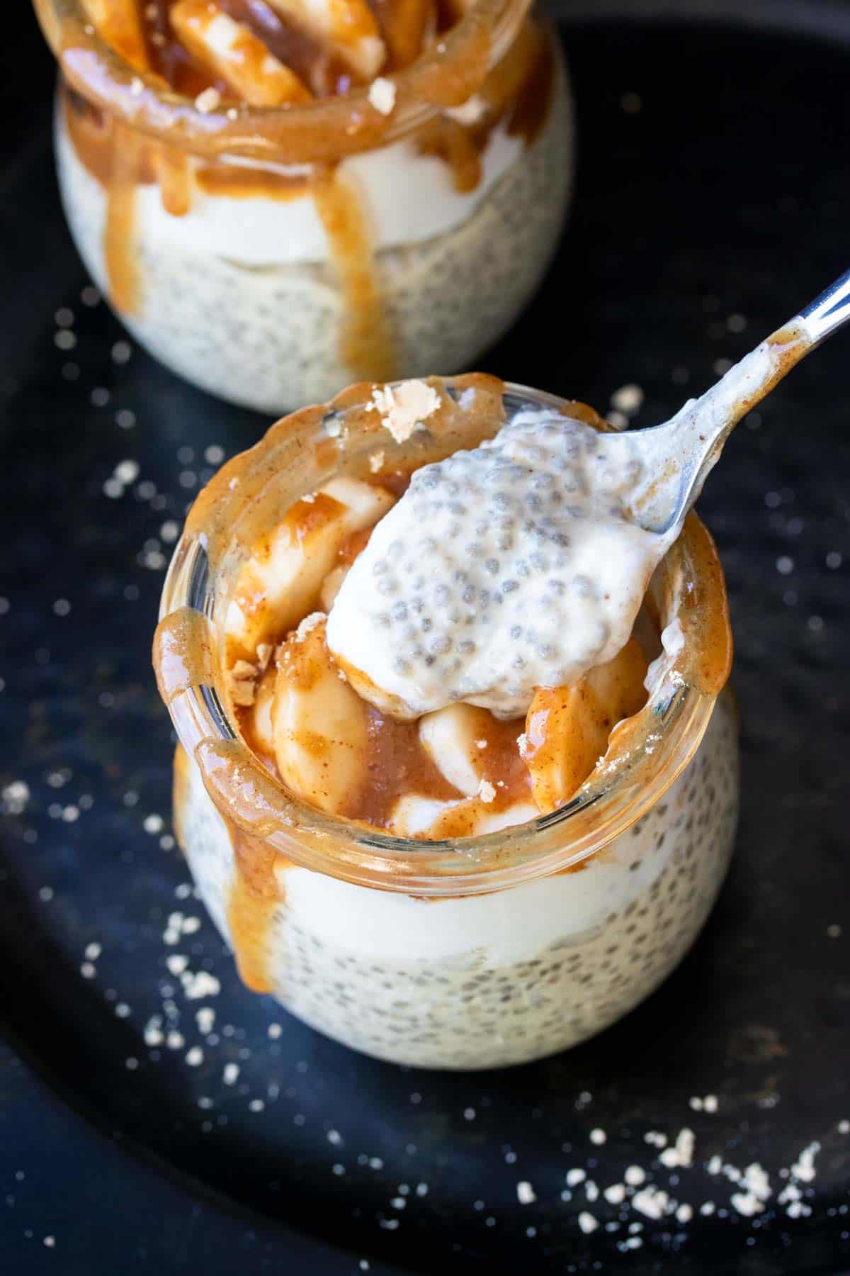 A spoon with chia pudding coming out of a jar with it topped with bananas and caramel.