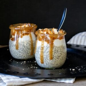 Two glass jars sitting on a black disc filled with chia pudding and topped with caramel.