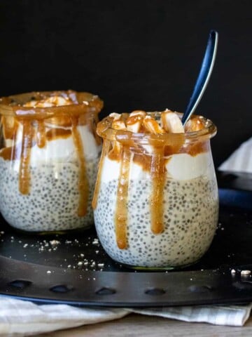 Two glass jars sitting on a black disc filled with chia pudding and topped with caramel.