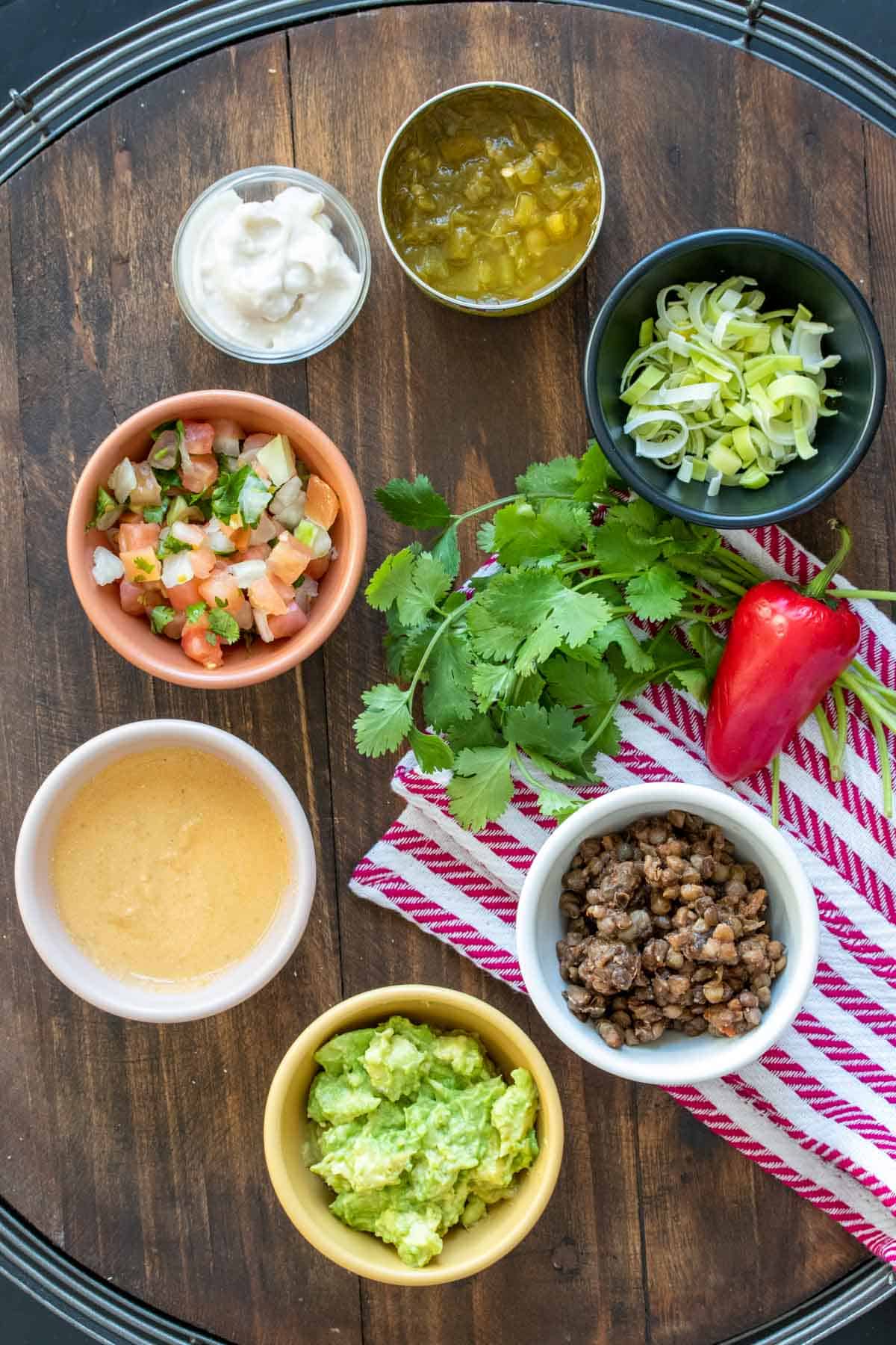 Top view of a wooden tray with bowls of ingredients for a Mexican 7 layer dip.