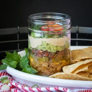 Layers of meat, cheese, chiles, salsa, guacamole, creamy sauce and garnish in a jar.