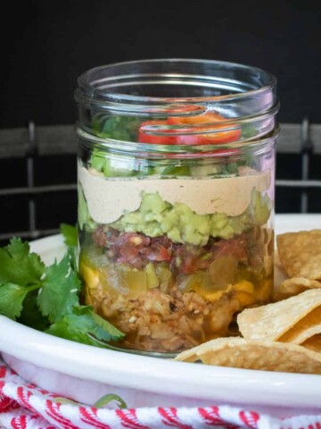 Layers of meat, cheese, chiles, salsa, guacamole, creamy sauce and garnish in a jar.