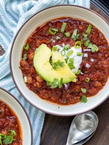 Cream bowl with chili inside topped with slices of avocado and green onions.