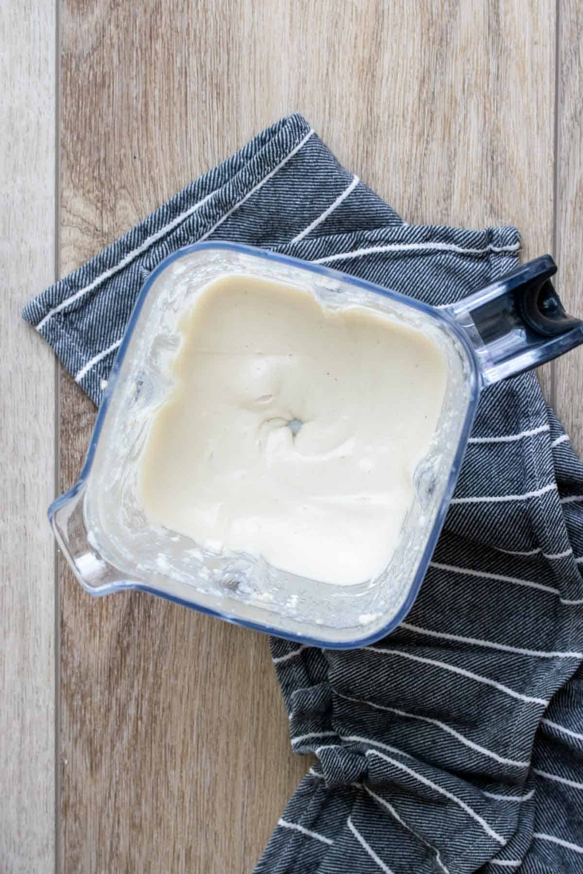 Top view of a blender on a blue towel with a creamy sauce inside