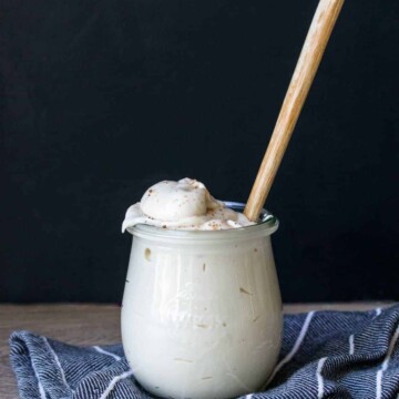 A glass jar filled with bechamel sauce sitting on a blue striped towel