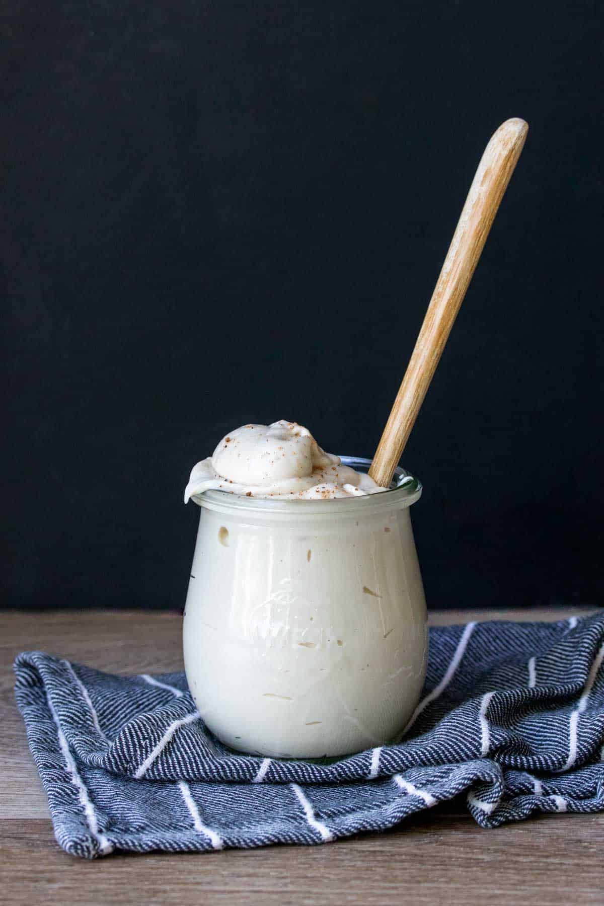 A glass jar filled with bechamel sauce sitting on a blue striped towel