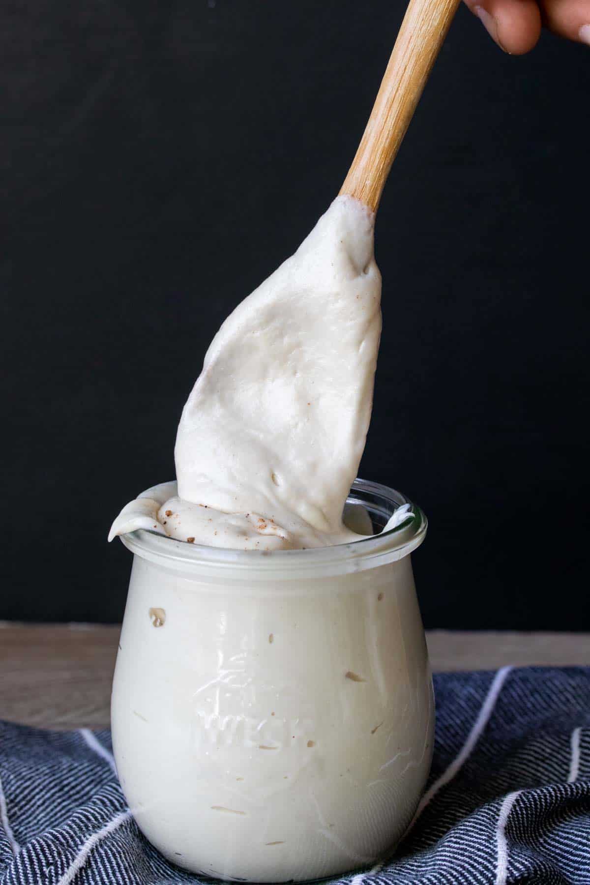 A wooden spoon coming out of a jar covered in a white sauce