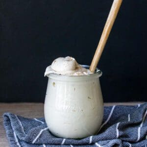 A glass jar filled with a creamy white sauce with a spoon in it.