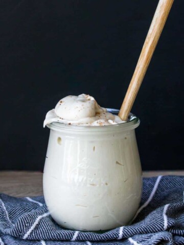 A glass jar filled with a creamy white sauce with a spoon in it.