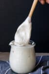 A glass container filled with a white creamy sauce and a wooden spoon coming out of it.