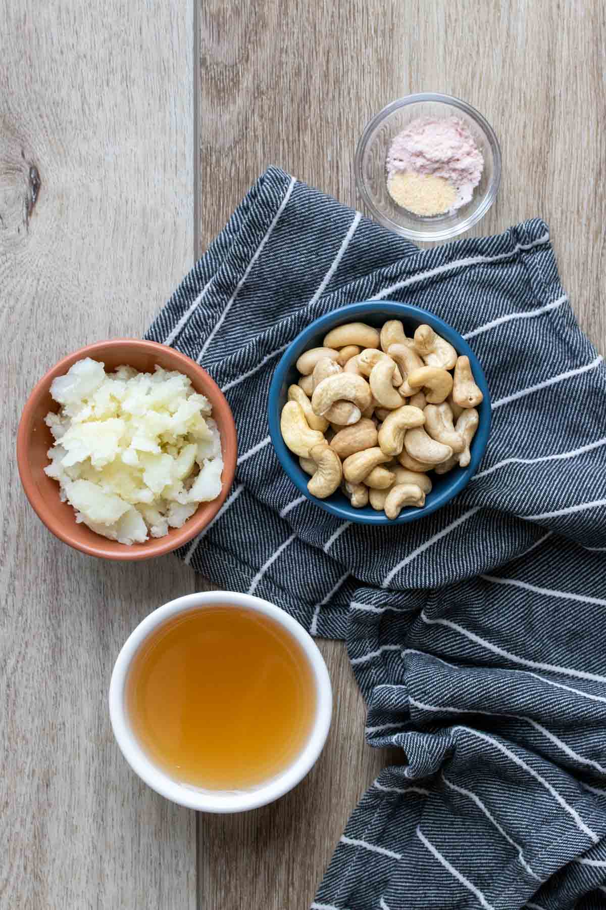 Bowls with cashews, potato, broth and salt on a blue striped towel on a wooden surface