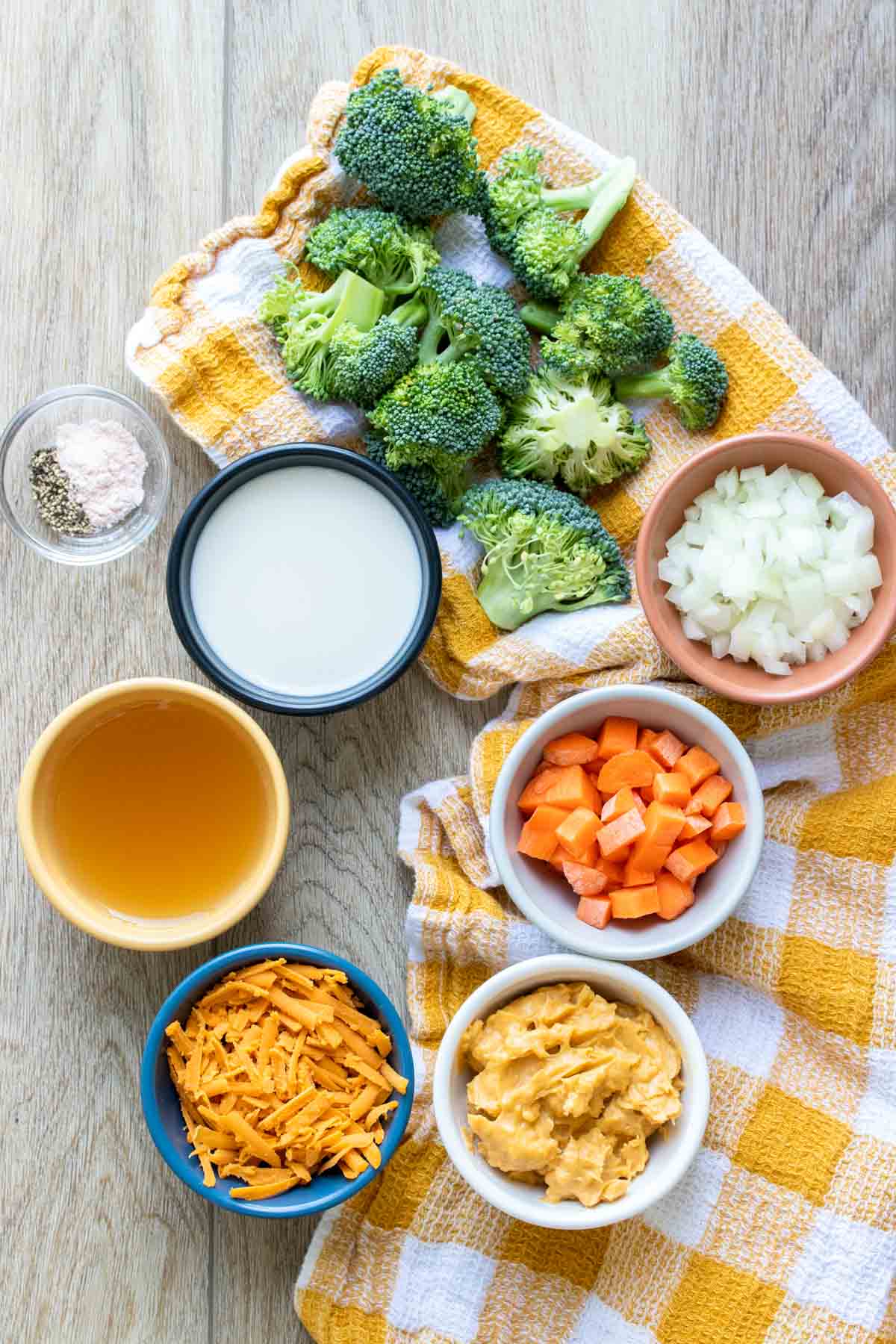 Top view of ingredients needed to make a broccoli cheddar soup sitting on a yellow checkered towel