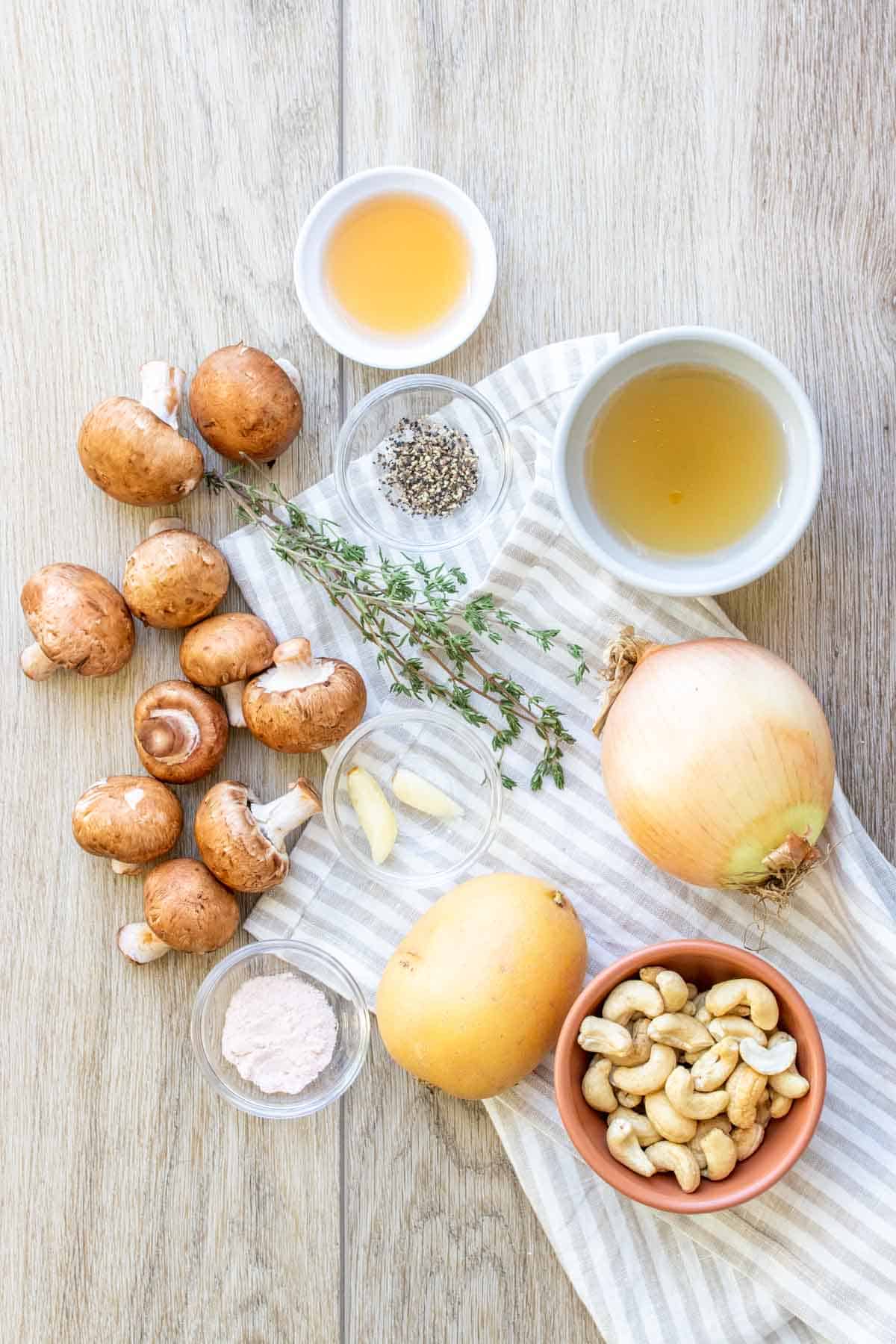 Ingredients on a wooden surface needed to make a cream of mushroom soup made dairy free with cashews and potato