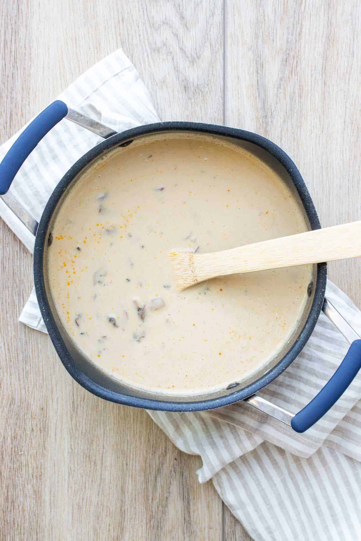 A wooden spoon mixing a creamy soup in a black pot on a tan striped towel