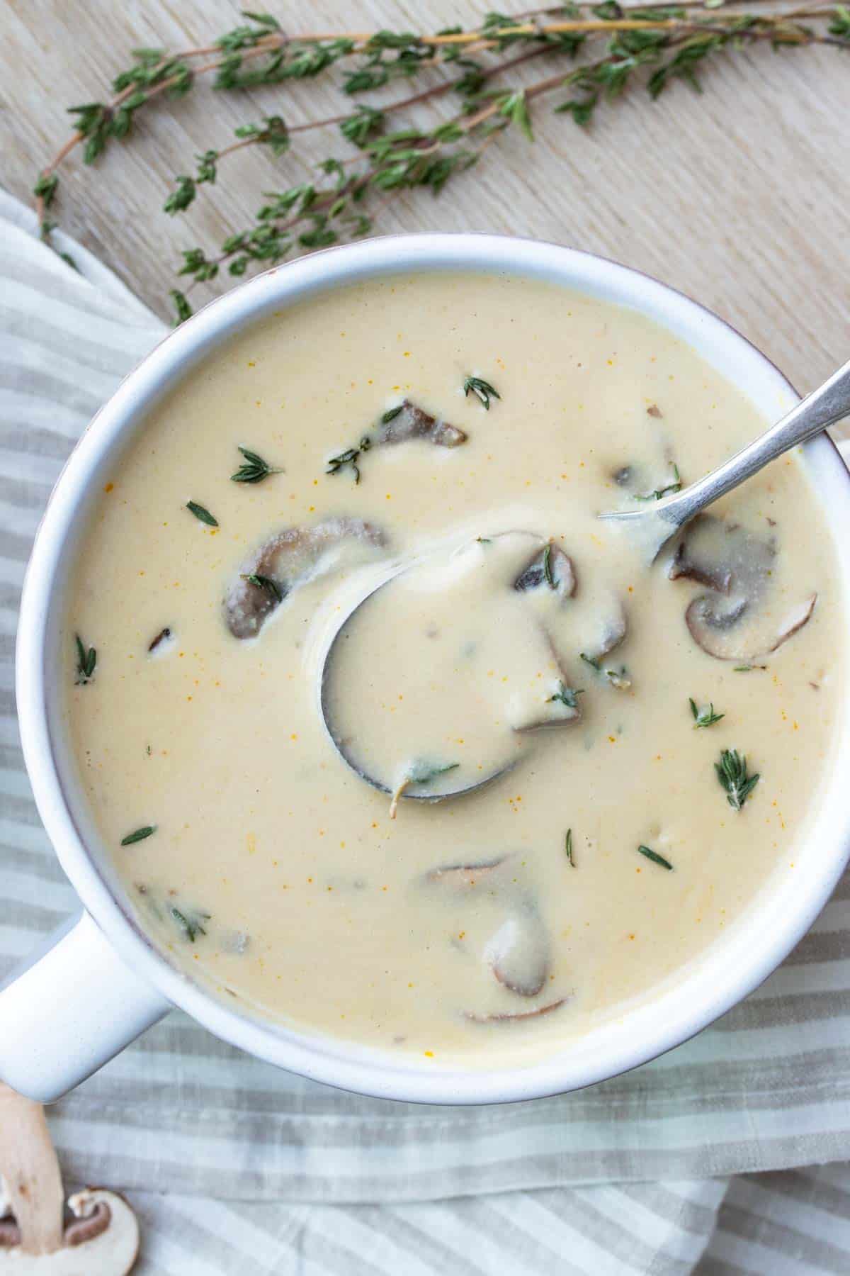 A spoon getting some cream of mushroom soup from a white bowl on a striped tan towel