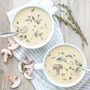 Top view of a creamy mushroom soup in two white soup bowls with thyme on top and on the side.