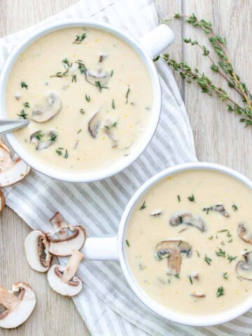 Top view of a creamy mushroom soup in two white soup bowls with thyme on top and on the side.