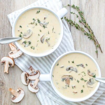 Top view of a creamy mushroom soup in two white soup bowls with thyme on top and on the side