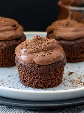 A white plate on a black plate topped with three chocolate cupcakes without liners sprinkled with chocolate shavings