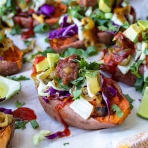 Front view of sweet potato skins on a white piece of parchment paper loaded with toppings.