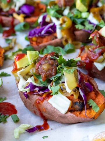 Front view of sweet potato skins on a white piece of parchment paper loaded with toppings.