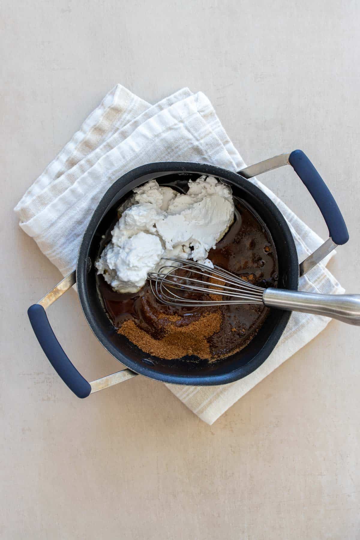 A whisk about to mix coconut cream, maple syrup and coconut sugar in a small pot