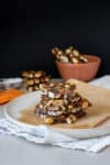 Peanut brittle stacked on a piece of parchment paper on top of a plate with more peanut brittle in the background.