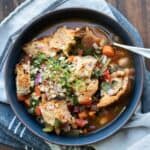 A black bowl with a veggie bean soup topped with chunks of bread.