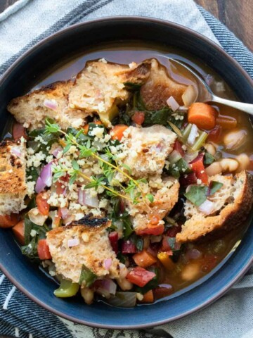 A black bowl with a veggie bean soup topped with chunks of bread.