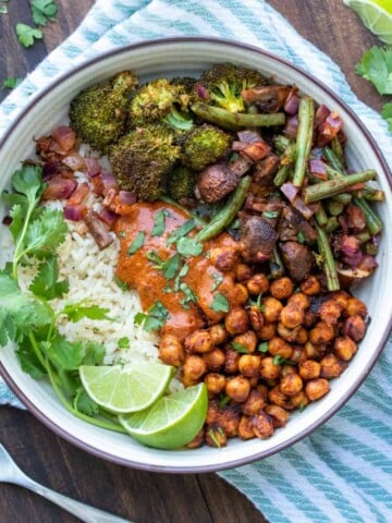 A bowl on a striped towel filled with veggies, chickpeas and rice with tikka masala sauce