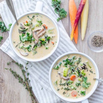 Two white soup bowls on a striped towel filled with creamy veggie and rice soup and topped with thyme