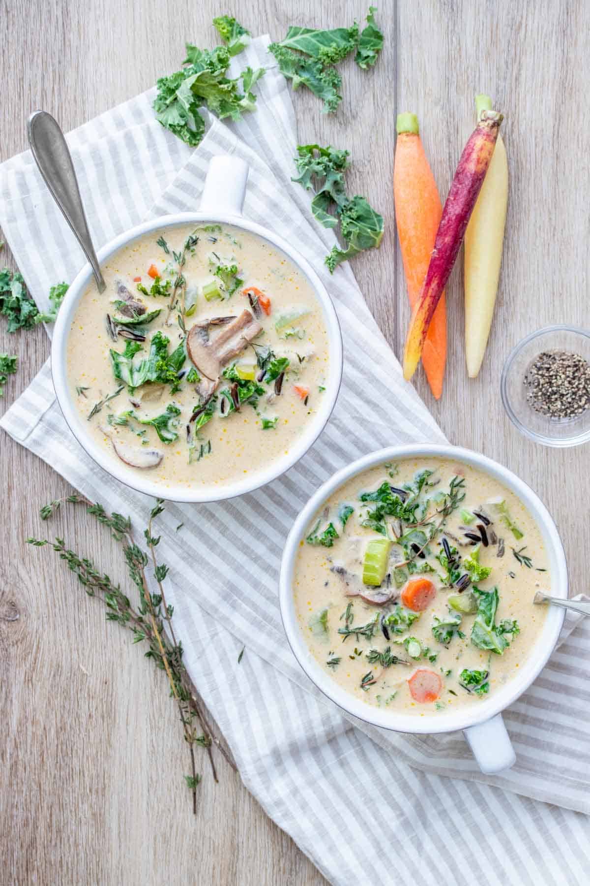 Two white soup bowls on a striped towel filled with creamy veggie and rice soup and topped with thyme.