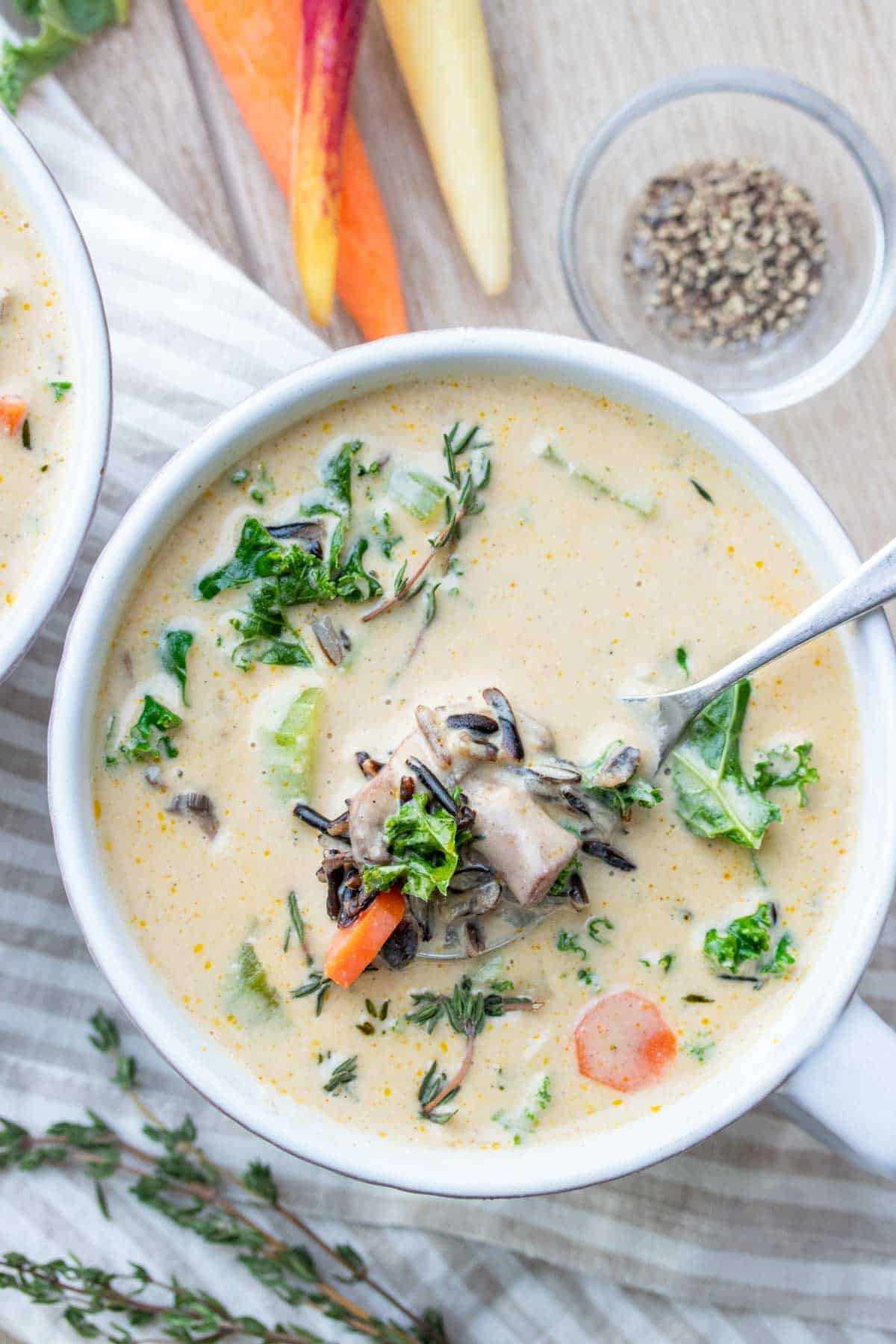 Spoon getting a bite of a creamy veggie and wild rice soup from a white soup bowl on a striped towel