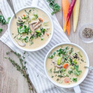 Two bowls of creamy veggie rice soup on a striped towel next to carrots, thyme and kale.