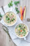 Two white soup bowls sitting on a striped towel on a light wooden surface with a rice and veggie soup inside.