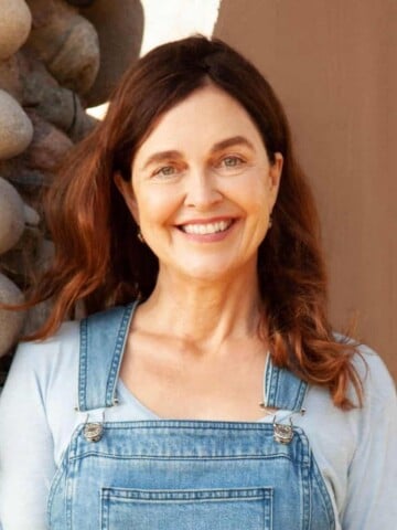 A woman with reddish brown hair in a white shirt and overalls smiling