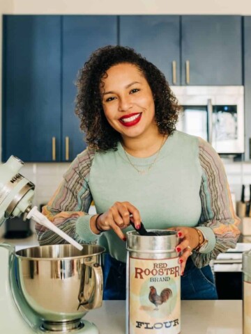 A woman in a mint green shirt with curly hair cooking in her kitchen