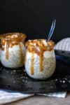 A glass jar filled with chia pudding, whipped cream and bananas topped with caramel